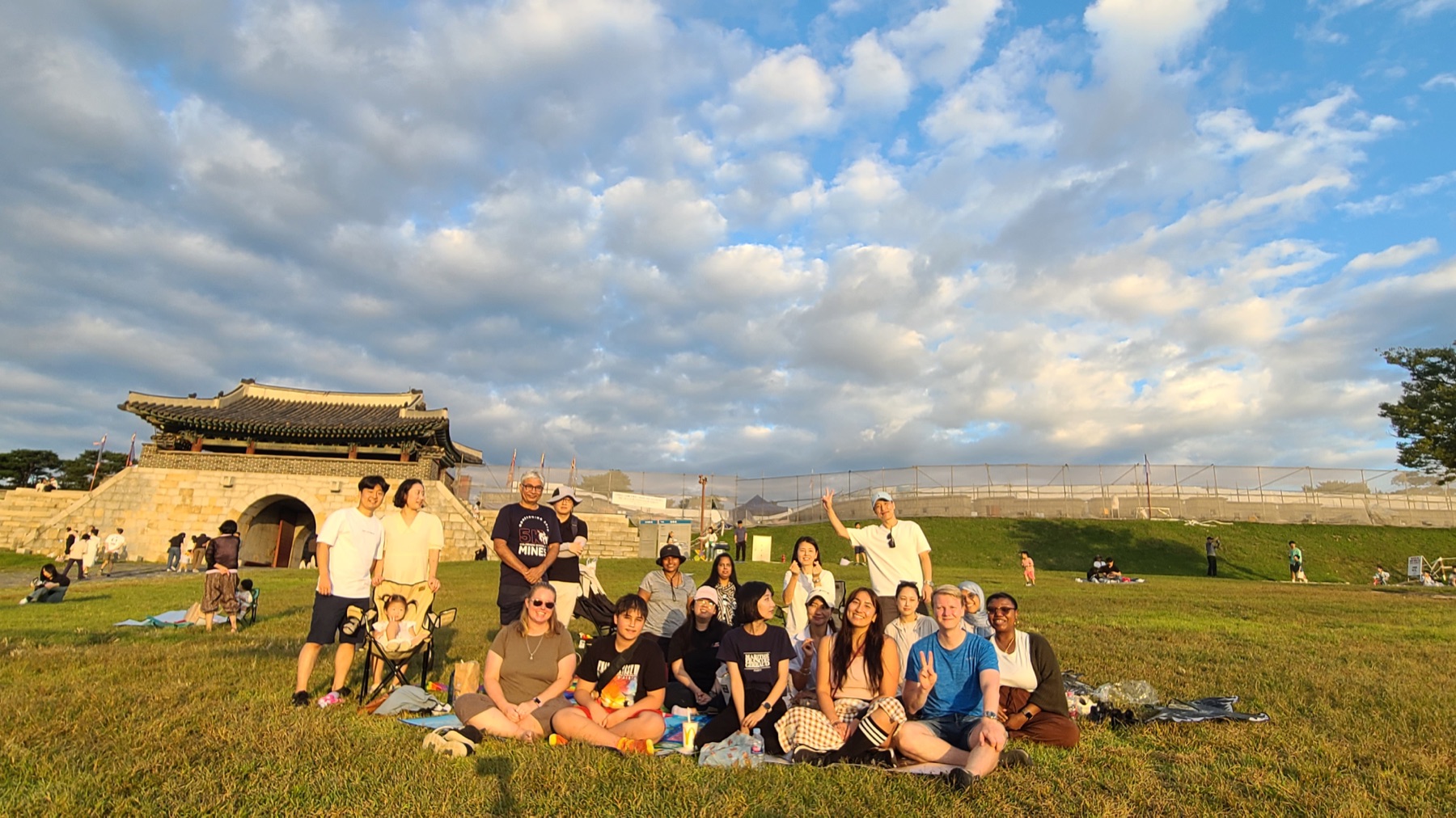 A Make A Circle community group gathered outdoors in Suwon during golden hour.